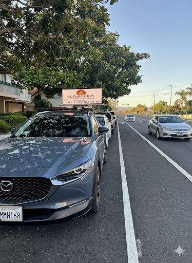 A Quantum Digital Topper glowing at dusk in a line of parked cars along a busy road